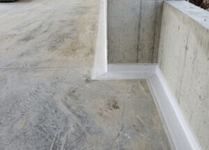 The coating forms a continuous protective barrier around the perimeter, including the internal corner and recessed section. Careful detailing at these wall-to-floor transitions helps reduce the risk of water penetration through vulnerable construction joints and concrete interfaces.